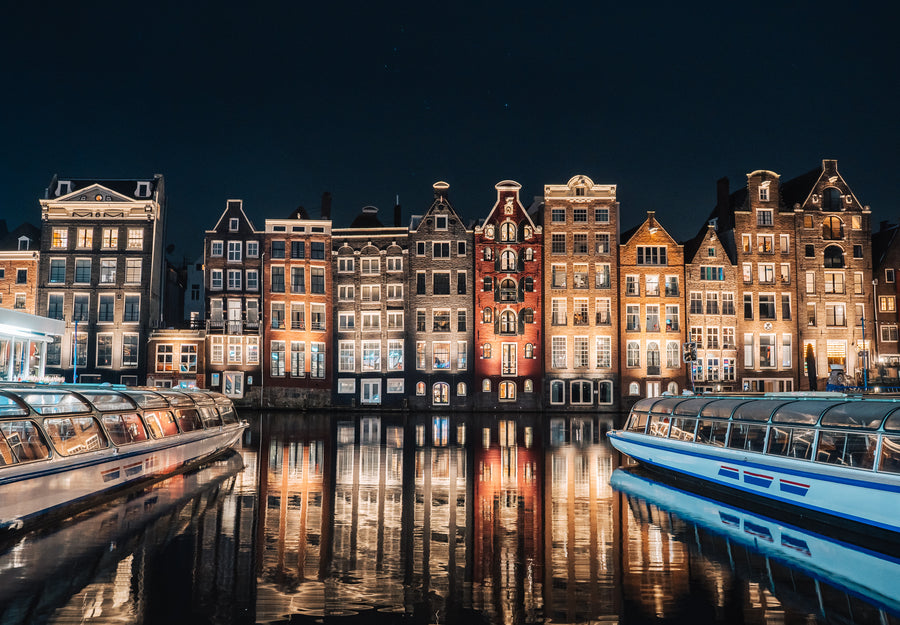 Verlichte grachtenpanden aan het Damrak die 's avonds weerspiegelen in het water, Amsterdam