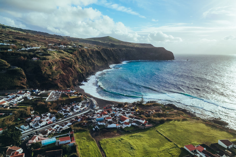 A village with white houses between green fields and the ocean in the Azores, seen from above