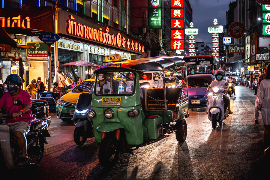 A tuk-tuk and scooters on a neon-lit street in Bangkok's Chinatown at night