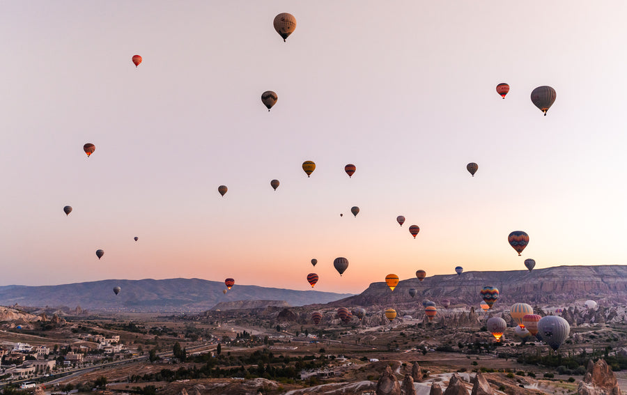 Dozens of hot-air balloons in a pink dawn sky over a valley in Cappadocia