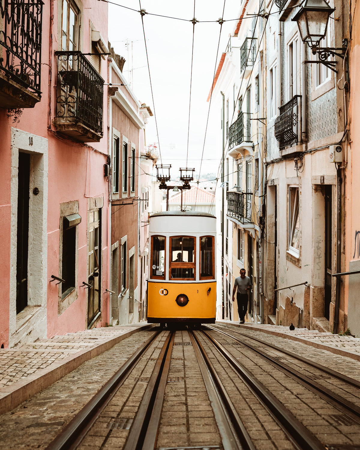 The yellow Bica funicular on a steep cobbled street between old houses in Lisbon