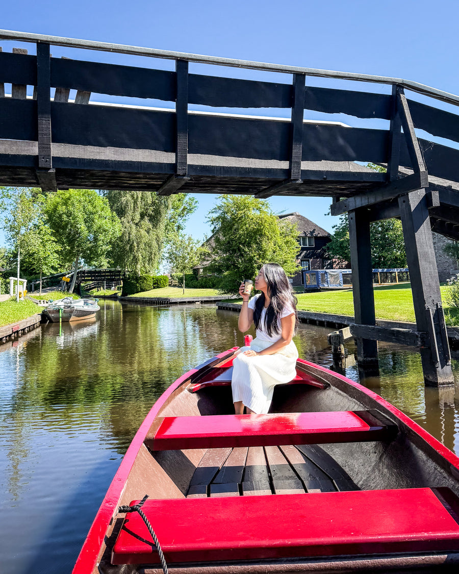 Een vrouw in een rode boot op een gracht onder een houten brug in Giethoorn