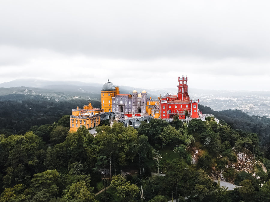 The red and yellow Pena Palace on a forested hilltop in Sintra, seen from above