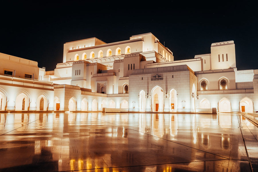 Royal Opera House Muscat lit up at night and reflected in the stone forecourt, Oman