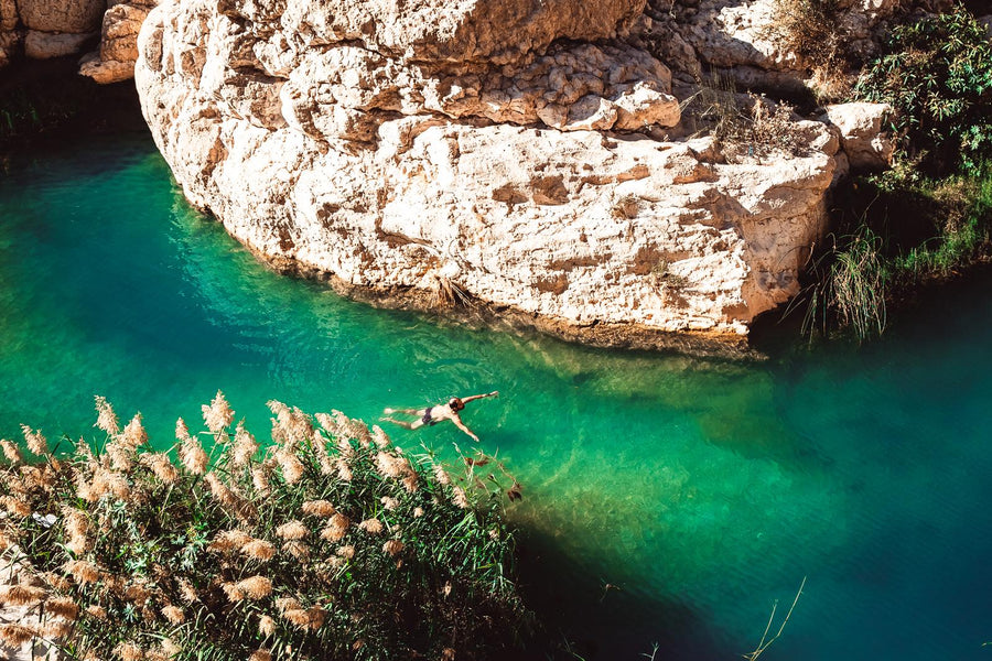 A swimmer in a turquoise pool below pale rocks in Wadi Shab, Oman